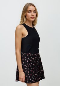 Schwarzes ärmelloses Oberteil mit rundem Ausschnitt, kombiniert mit einem schwarzen Rock mit einem floralen Muster in Rosa und Weiß sowie einem plissierten Design.