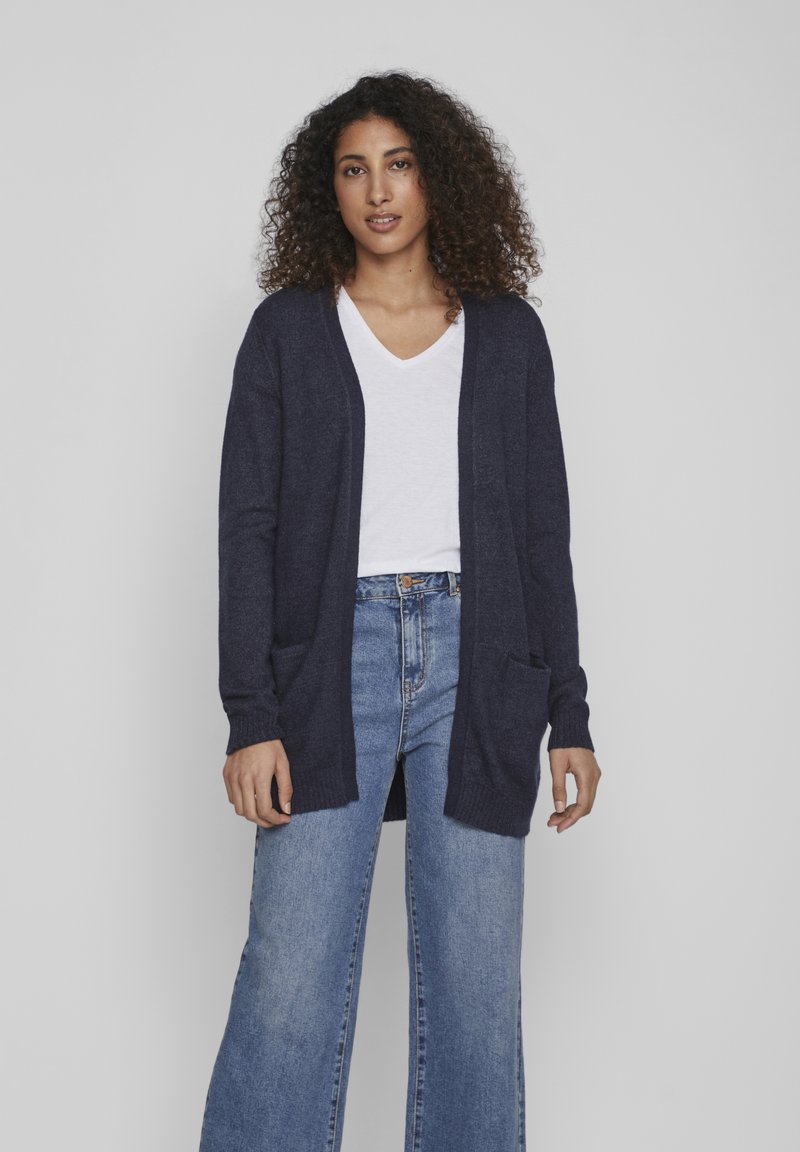 Navy knit cardigan with long sleeves, open front, two pockets, and ribbed cuffs, paired with a white V-neck t-shirt and high-waisted jeans.