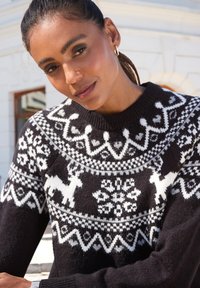 Schwarzer Strickpullover mit weißen Mustern von Rentieren und Schneeflocken, runder Ausschnitt, strukturierter Stoff mit gerippten Bündchen.