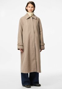 Cappotto di lana beige con ampio colletto, maniche lunghe e tasche frontali; presenta dettagli sui polsini con bottoni e una silhouette dritta.