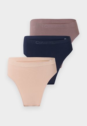 Három varrás nélküli Calvin Klein magas kivágású alsónadrág bézs, tengerészkék és mályva színekben, egymásra helyezve egy világosszürke háttér előtt.