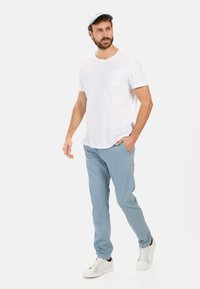 Witte T-shirt met korte mouwen en een borstzak, gecombineerd met lichtblauwe broek en witte sneakers, alles op een effen achtergrond.