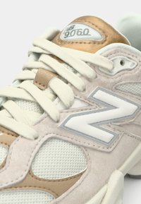 Pantof sport ușor bej și crem, realizat din plase și piele intoarsă. Are un accent de piele intoarsă culoarea nisipului, logo alb și șireturi bej. Formă rotunjită.