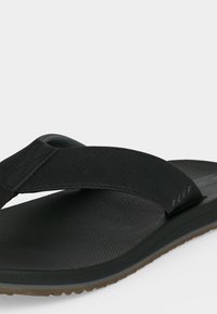 Μαύρο σανδάλι τύπου φλιπ φλοπ με υφασμάτινο λουράκι, υφή στην πάτημα, ρυθμιζόμενο κλείσιμο με βέλκρο και καφέ λαστιχένια σόλα.