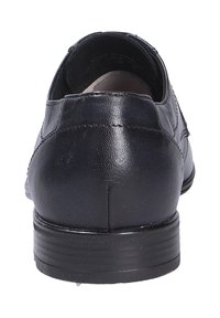 Chaussure en cuir noire avec une texture lisse, un talon arrondi et des coutures discrètes à l'arrière. Profil bas avec une semelle en caoutchouc robuste.