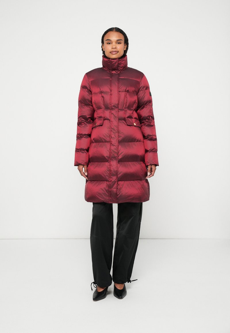 Burgundská péřová bunda s vysokým límcem, horizontálním prošíváním, dvěma předními kapsami a staženým pasem. Kombinováno s černými kalhotami.