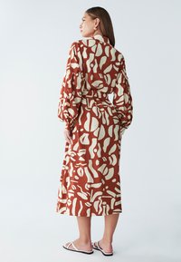 duga haljina rđeće smeđe boje s apstraktnim kremastim uzorcima, dugim rukavima i pojasom u struku. Glatka tekstura i dizajn do telećeg dijela nogu.