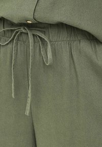 Olivengrønne linnedbukser med elastisk taljebånd og bundet snøre, kombineret med matchende linnedtop med træknapper.