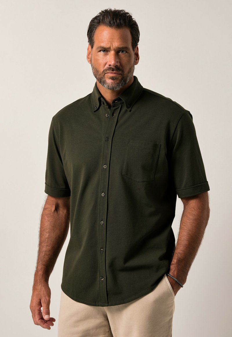 Camisetta button-up verde scuro con maniche corte e tasca. Materiale morbido, colletto strutturato e vestibilità rilassata. Cuciture rinforzate sulle cuciture.