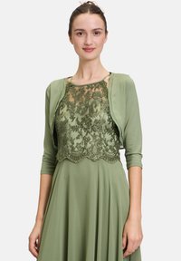 Zielona sukienka z koronką z haftem kwiatowym i falbaniastym wykończeniem. Krótkie rękawy i gładka tkanina tworzą warstwowy wygląd.