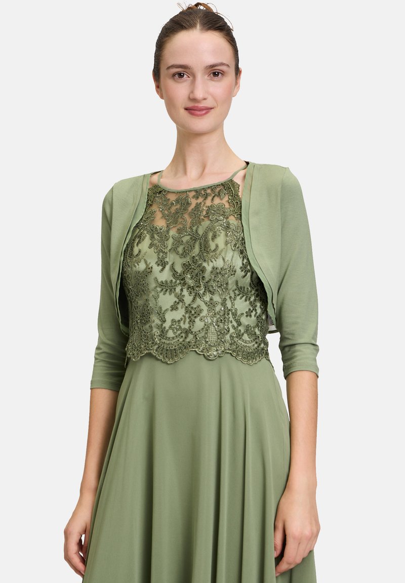 Zielona sukienka z koronką z haftem kwiatowym i falbaniastym wykończeniem. Krótkie rękawy i gładka tkanina tworzą warstwowy wygląd.