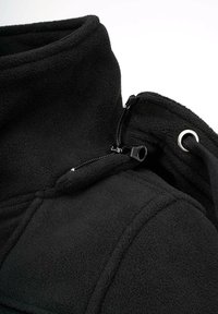 Črna flis jakna z visokim ovratnikom, zadrgo in nastavljivim vrvico. Mehka tekstura z detajli šivov in kovinsko zanko.