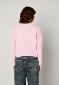 Rožinė pūkuota megztinis su ilgomis rankovėmis ir apvalia iškirpte, derinama su nublukusiais mėlyniais džinsais, turinčiais dvi galines kišenes. Paviršius atrodo minkštas ir pūkuotas.