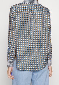 Camicia a fantasia in blu, marrone e bianco con design geometrico; maniche lunghe con dettagli ai polsini; tessuto morbido; vestibilità ampia; orlo curvo.