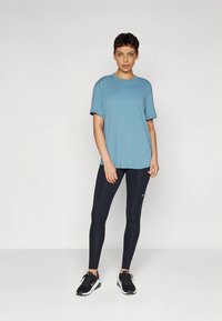 Lyseblå t-skjorte med korte ermer kombinert med svarte leggings, med en logo, og fullført med svarte treningssko.