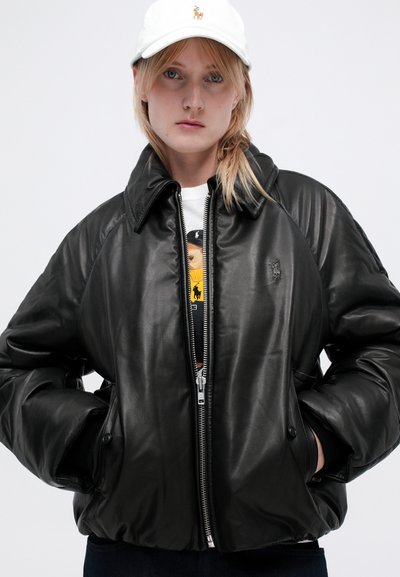 Černá kožená bomber bunda s vysokým límcem, zipovým zapínáním a bočními kapsami. Obsahuje logo na hrudi a pletené manžety.