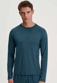 Teal lange mouw shirt met een ronde halslijn, gemaakt van textuurstof. Heeft raglanmouwen en een relaxte pasvorm. Eenvoudig ontwerp zonder patronen.