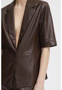 Blazer en cuir marron à manches courtes, décolleté en V profond et fermeture à un bouton. Présente une texture lisse et un design ajusté.