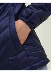 Námořnická modrá péřová bunda s prošívanou texturou a elastickými manžetami. Obsahuje boční kapsu s hladkým povrchem. Lehký a pohodlný design.