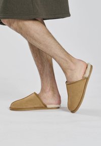 Bruine suède slippers met een zachte bontvoering, open achterkant en ronde neus. Kenmerken zijn een gladde, gestructureerde bovenkant en een duurzame zool.