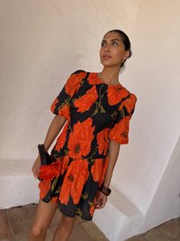 Abito nero con grandi motivi floreali arancioni, maniche a palloncino corte, vita aderente e gonna svasata. Il tessuto testurizzato aumenta l'interesse visivo.