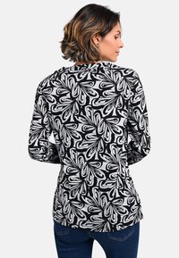 Schwarz-weißer Langarmshirt mit einem wirbelnden Blumenmuster. Weicher Stoff mit lockerer Passform, abgerundetem Saum und Rundhalsausschnitt.