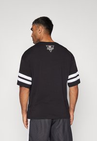 Tricou din bumbac negru cu dungi albe pe mâneci. are un logo triunghiular pe spate. Design simplu cu o croială lejeră.