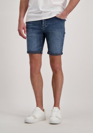 Donkerblauwe denimshorts met opgerolde zoom. Gekocht met witte sneakers voor een casual, aansluitende look. Middelmatige lengte tot aan de bovenbenen.