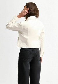 Vit croppad denimjacka med långa ärmar, knäppbara manschetter och söm i ryggen, kombinerad med högmidjade svarta raka jeans.