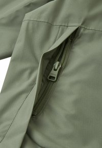 Olive green fabric with a smooth texture, featuring a zippered pocket and tonal stitching. The zipper has a pull tab marked "reima."