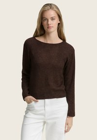 Pull marron avec un large col rond et des manches longues, fabriqué en matériau doux. Assorti à un pantalon blanc pour le contraste.