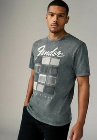 Heather gray t-shirt made of cotton, featuring a Fender graphic with amplifier designs in white and dark gray, round neckline, short sleeves.