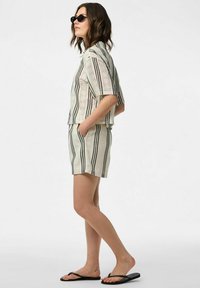 Completo leggero a due pezzi con maniche corte e pantaloni corti. Base crema con strisce verticali nere. Infradito neri e occhiali da sole.