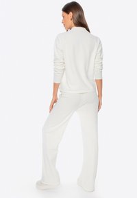 Completo da casa in pile bianco composto da una maglia a maniche lunghe e pantaloni larghi. Tessuto morbido con design minimalista, cuciture visibili e polsini a coste.