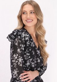 Czarna sukienka w kwiaty z falbaniastymi akcentami na ramionach, przezroczystym materiałem i dekoltem w serek. Posiada delikatny szary wzór kwiatowy na całej powierzchni.