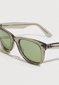 Γυαλιά ηλίου Ray-Ban με διαφανές γκρι σκελετό, πράσινους φακούς και ασημί διακοσμήσεις· διαθέτουν το χαρακτηριστικό λογότυπο στα πλαινά.