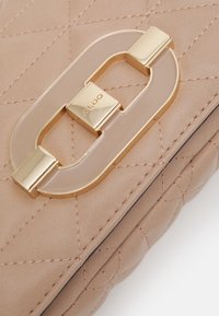 Rosa quiltad syntetisk väska med ett lås i guld och transparent akryl. Tydlig sömnadsdetalj synlig på ytan.