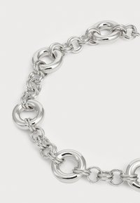 Bracciale in argento con anelli circolari lucidi e segmenti di catena intrecciati. Texture liscia con misure di anelli diverse.