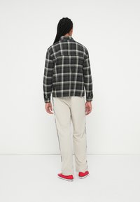 Camicia flanella a scacchi in bianco e nero con maniche lunghe, abbinata a pantaloni leggeri color beige e sneakers rosse, vista da dietro.