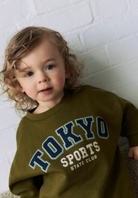Zelená bavlněná mikina s potiskem "TOKYO SPORTS STATE CLUB" v modré a bílé barvě, kulatým výstřihem a volným střihem.