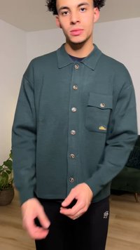 Camicia verde scuro con bottoni e colletto, caratterizzata da una tasca sul petto, tessuto strutturato e grandi bottoni.