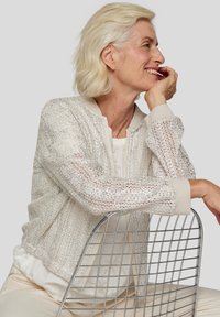 Silberne metallische Bomberjacke mit leichtem Strickdesign, gerippten Bündchen und einem kontrastierenden beigen Kragen, kombiniert mit einem neutralen Oberteil.