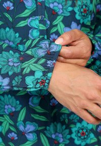 Bluse mit Floral-Muster auf dunkelblauem Hintergrund, mit lebhaften grünen und blauen Blumen sowie einem Knopfverschluss am Kragen.