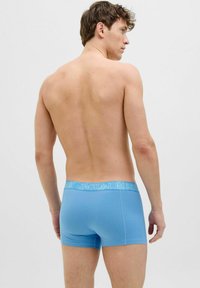 Blue boxer shorts made of soft fabric with a contrasting white logo waistband, fitted shape, and minimal design.