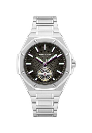 Zilverkleurig roestvrijstalen Kenneth Cole horloge met zwarte gestructureerde wijzerplaat, luminieuze wijzers, uurmarkeringen en zichtbare automatische beweging op 6 uur.