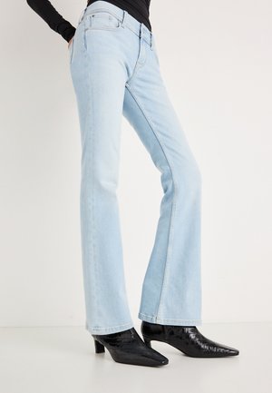 Vaqueros acampanados azul claro hechos de denim, con diseño clásico de cinco bolsillos y ligero desgaste sutil. Combinados con botines negros texturizados.