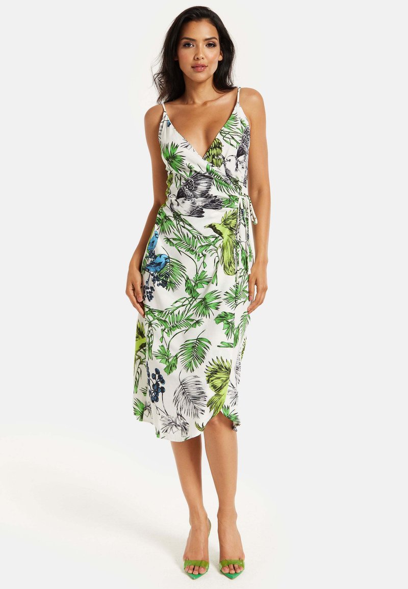 Wrap dress with a V-neck and adjustable tie, featuring a floral pattern in green and blue on white fabric. Paired with green heels.