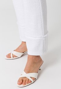 Witte textuurbroek met een ruwe zoom, gecombineerd met witte open-teense sandalen met gekruiste banden en een kleine hak.