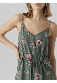 Květinový overal v zelené barvě, s výstřihem do V, tenkými ramínky a elastickým pasem na šňůrku. Ozdobený růžovými a fialovými květy.