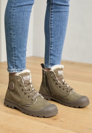 Olivgrüne Knöchelstiefel mit Wildleder- und Kunstfellfutter, Gummisohlen, seitlichem Reißverschluss und rundem Logo. Tragen zu blauen Skinny Jeans.